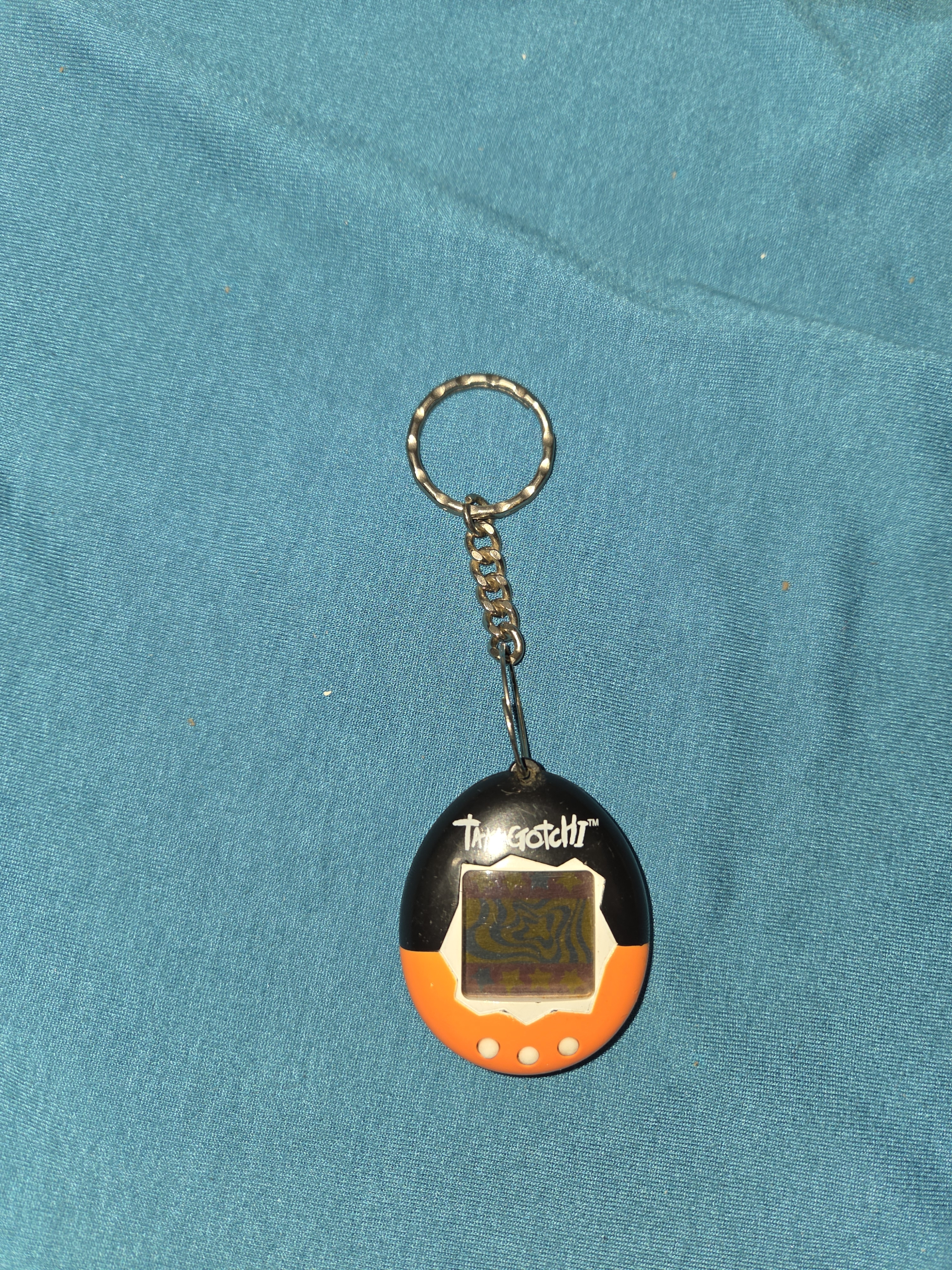 1997 Bandai Tamagotchi virtual pet in an orange and black egg shell with a grey monochrome screen and three buttons